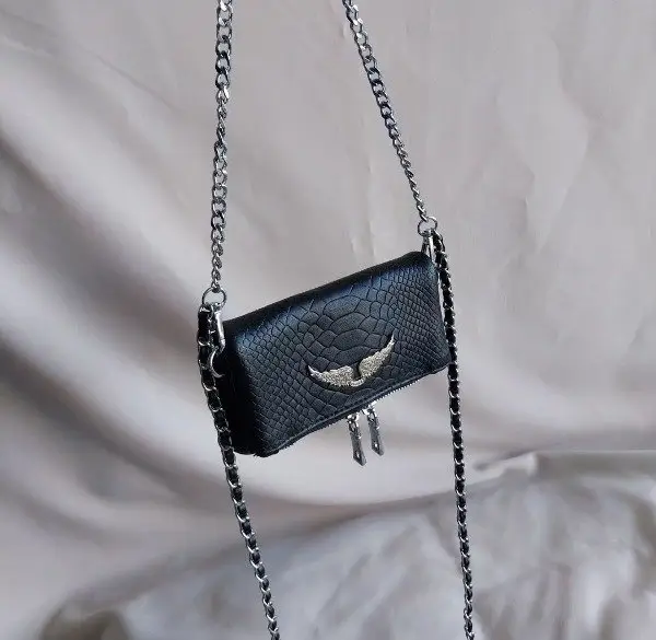 Cartera bandolera negra con diseño de reptil y cadena plateada. Ideal para un look rocker y canchero. Perfecta para llevar lo esencial con estilo.